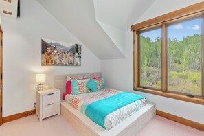 A bedroom with a bed, a nightstand, a lamp, a painting, and a window with a view of trees. - The Overlook Telluride- Includes 2 Ski Passes (Mountain Village)
