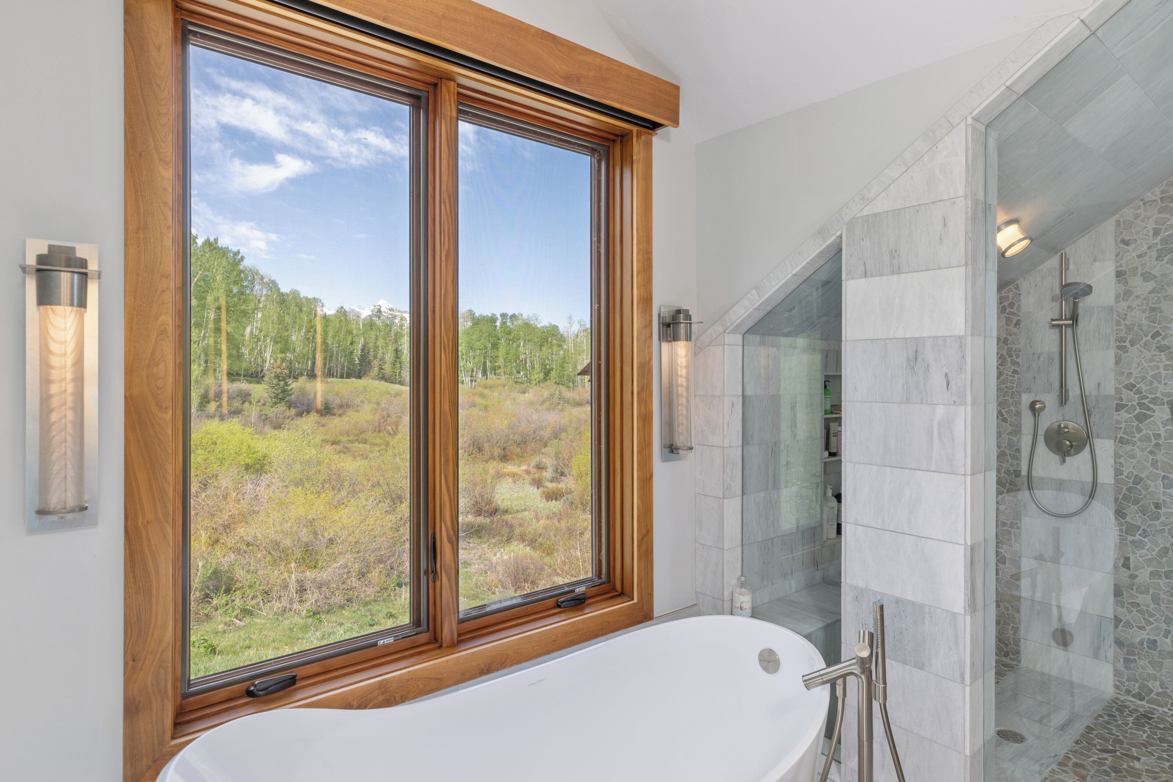 A bathroom with a large window, a freestanding bathtub, and a glass-enclosed shower area.