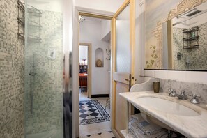 Un baño con cabina de ducha de vidrio, un lavamanos blanco sobre encimera de mármol y un espejo con marco decorativo.