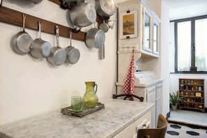 A kitchen with hanging pots, a marble countertop, a red and white checkered towel, and a view of the outside through a window. - Colosseo The Family Home in Monti (Roma)