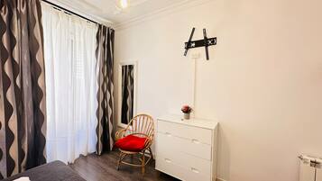 A bedroom with a bed, a chair, a dresser, a mirror, and a wall-mounted light fixture.