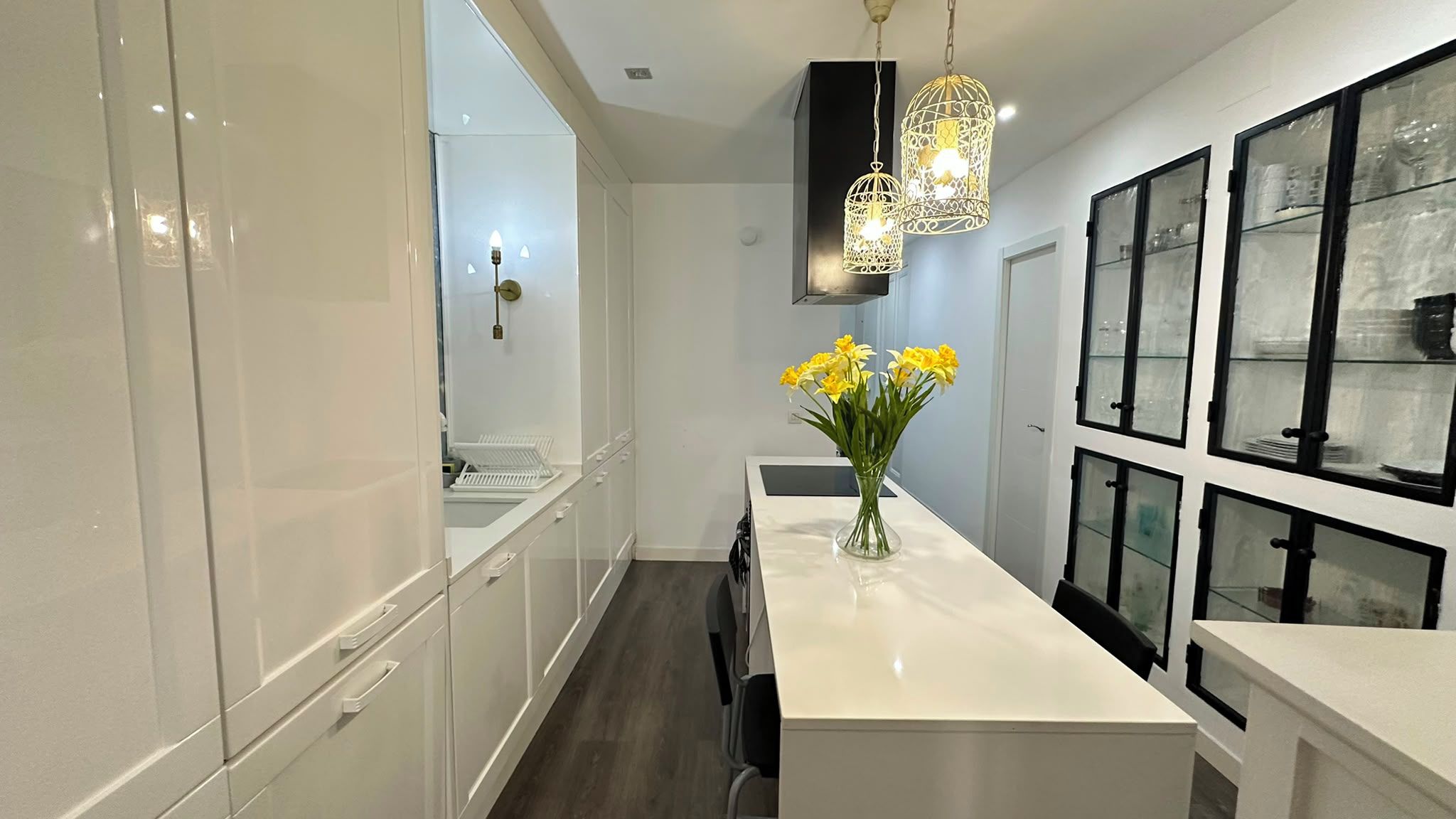 A modern kitchen with white cabinetry, a central island, and a vase with yellow flowers.