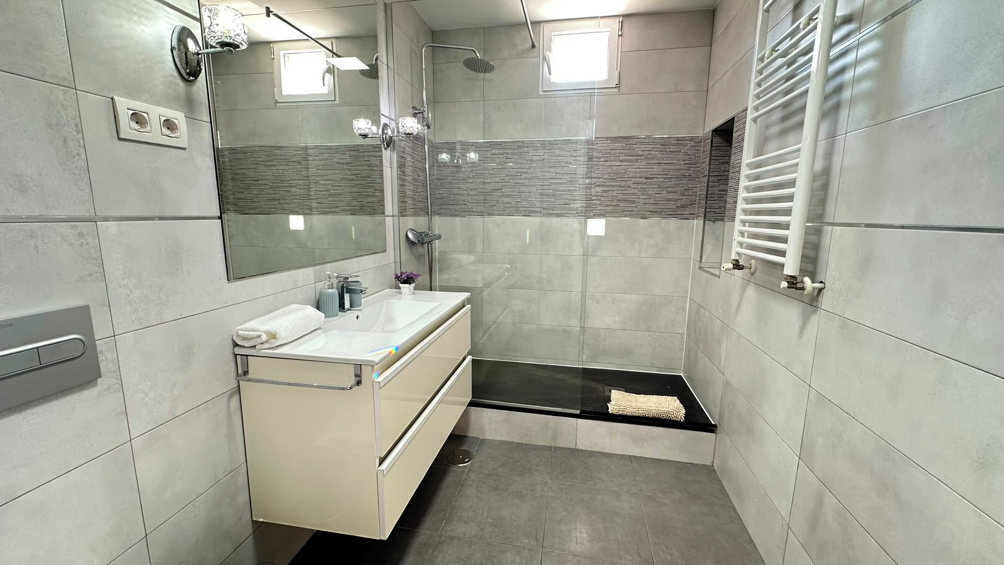 Un baño moderno con ducha, lavamanos con espejo y un perchero para toallas.