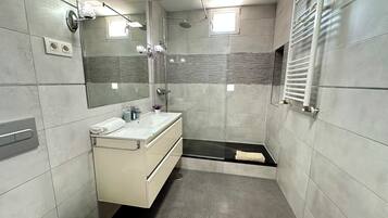 Un baño moderno con ducha, lavamanos con espejo y un perchero para toallas.