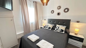 A neatly arranged hotel room with a bed, two bedside tables, a television, and decorative wall clocks. - Rooms Cabeza (Madrid)