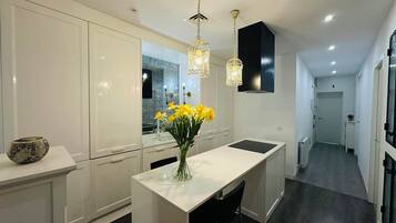 Een moderne keuken met witte kasten, een centraal eiland met een vaas gele bloemen, en hanglampen.