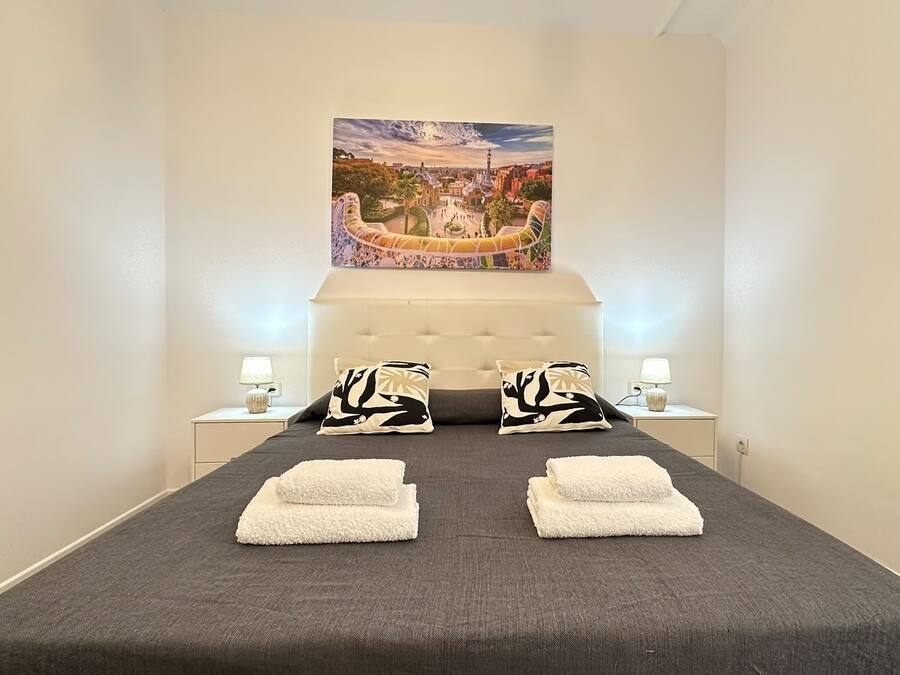 Quarto de hotel com uma cama, duas mesas de cabeceira com abajures, um quadro grande acima da cama e vista para um edifício pela janela.