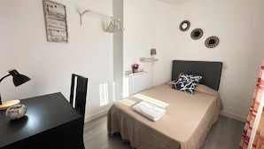 A bedroom with a bed, a desk, a chair, a bedside table, a lamp, and wall decorations. - Rooms Cabeza (Madrid)