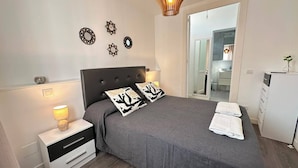 A bedroom with a bed, bedside tables, a nightstand, a lamp, and a view of a bathroom. - Rooms Cabeza (Madrid)