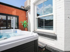A hot tub adjacent to a white brick building with a large window. - The Lodge (Shrewsbury)