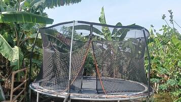 Un trampolín con red de seguridad en un espacio exterior con vegetación.
