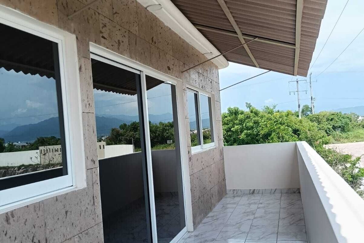 A balcony with a tiled floor and large windows offering a view of the landscape.