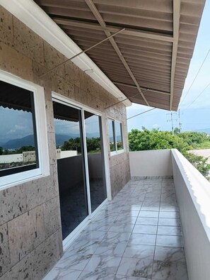A balcony with a tiled floor and large windows offering a view of the landscape.