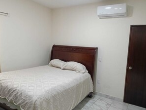 Un dormitorio con cama, una puerta y un equipo de aire acondicionado.