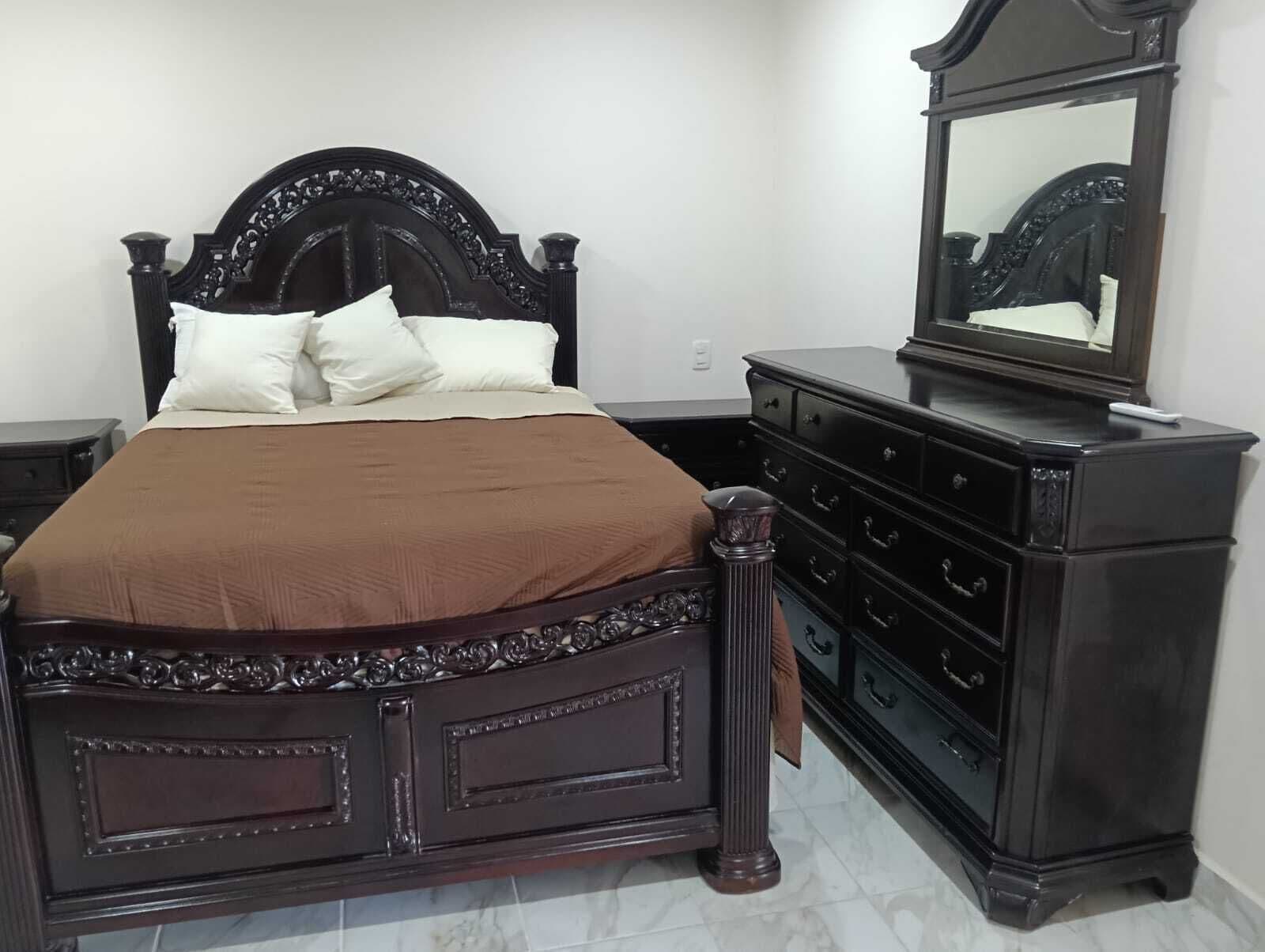 Une chambre à coucher avec un lit en bois foncé, des oreillers blancs, une couvre-lit marron, une commode et un miroir.