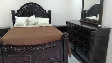 Une chambre à coucher avec un lit en bois foncé, des oreillers blancs, une couvre-lit marron, une commode et un miroir.