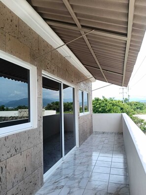 Un balcón con vistas al paisaje, un espacio cubierto con techo metálico y suelo de baldosas.