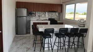 Una cocina moderna con encimera de mármol, un refrigerador y una zona de comedor con taburetes de bar.