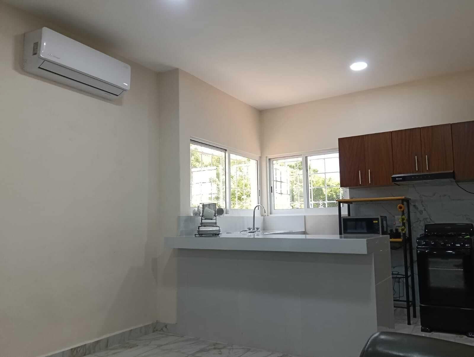 A kitchen with a built-in stove, a microwave, and a sink. There are windows providing natural light and a view of the outside.
