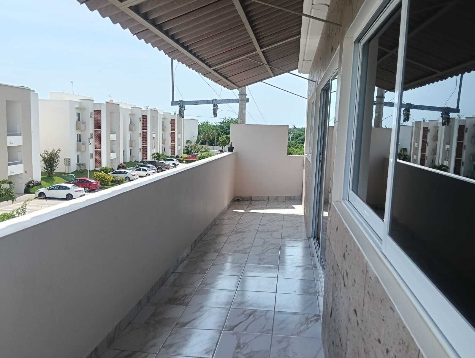 Un balcon doté d’un sol carrelé, d’une rambarde en métal et offrant une vue sur les voitures garées et les bâtiments en arrière-plan.