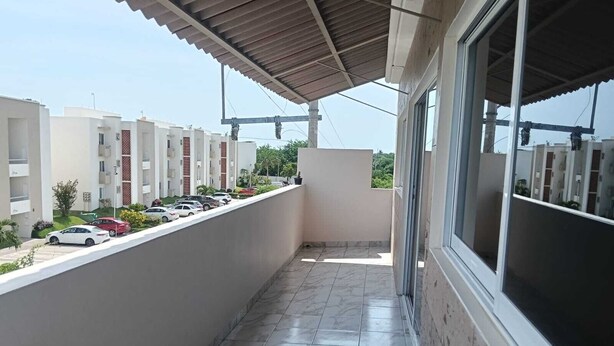 Un balcón con piso de baldosas, barandilla de metal y vista a coches estacionados y edificios al fondo.