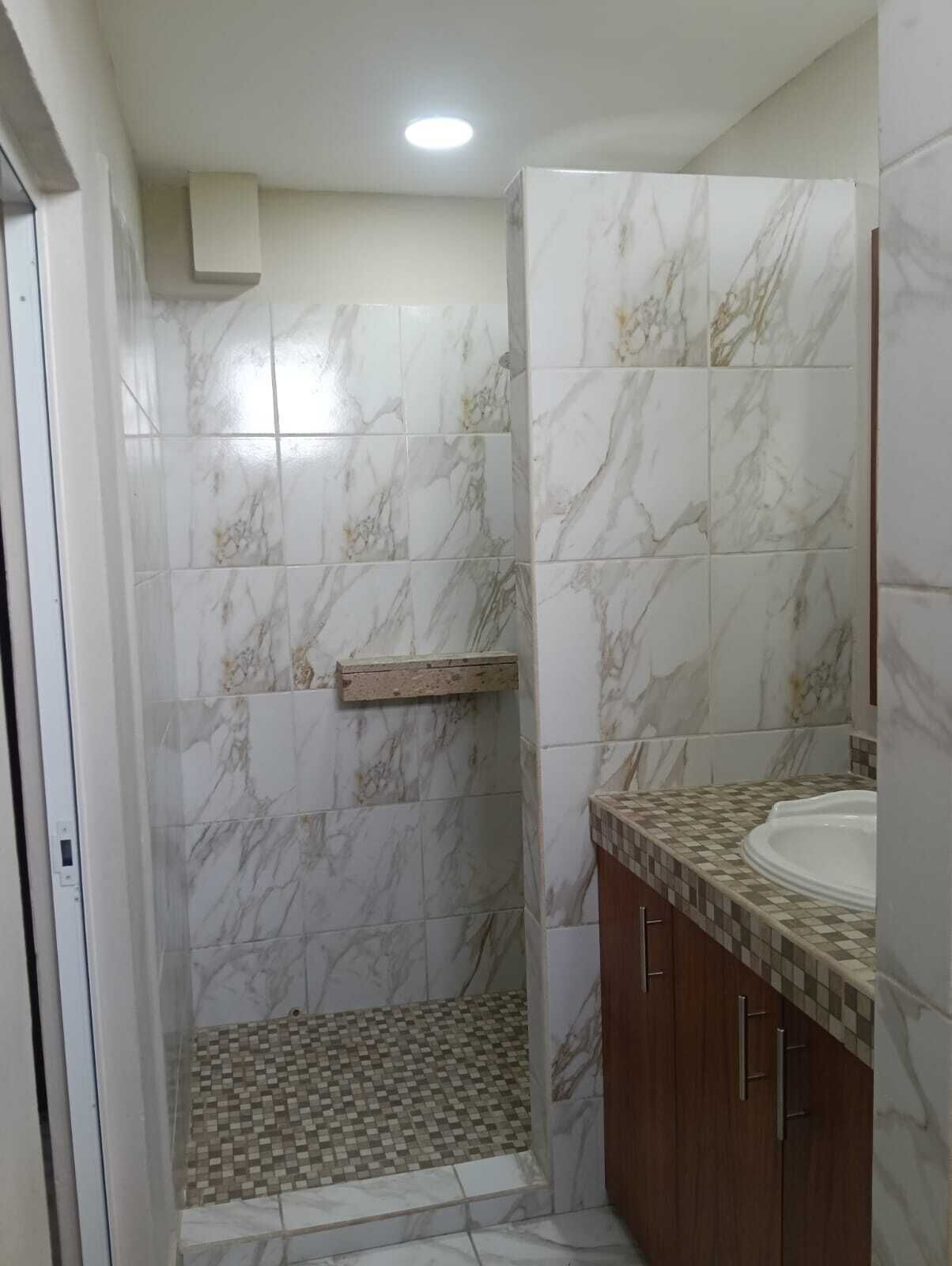 A bathroom with a shower, tiled walls, a checkered floor, and wooden cabinets.