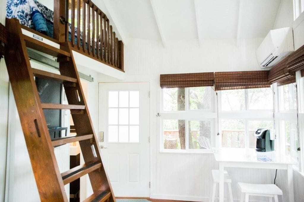 A room with a loft bed, a desk with a chair, and a window with blinds.