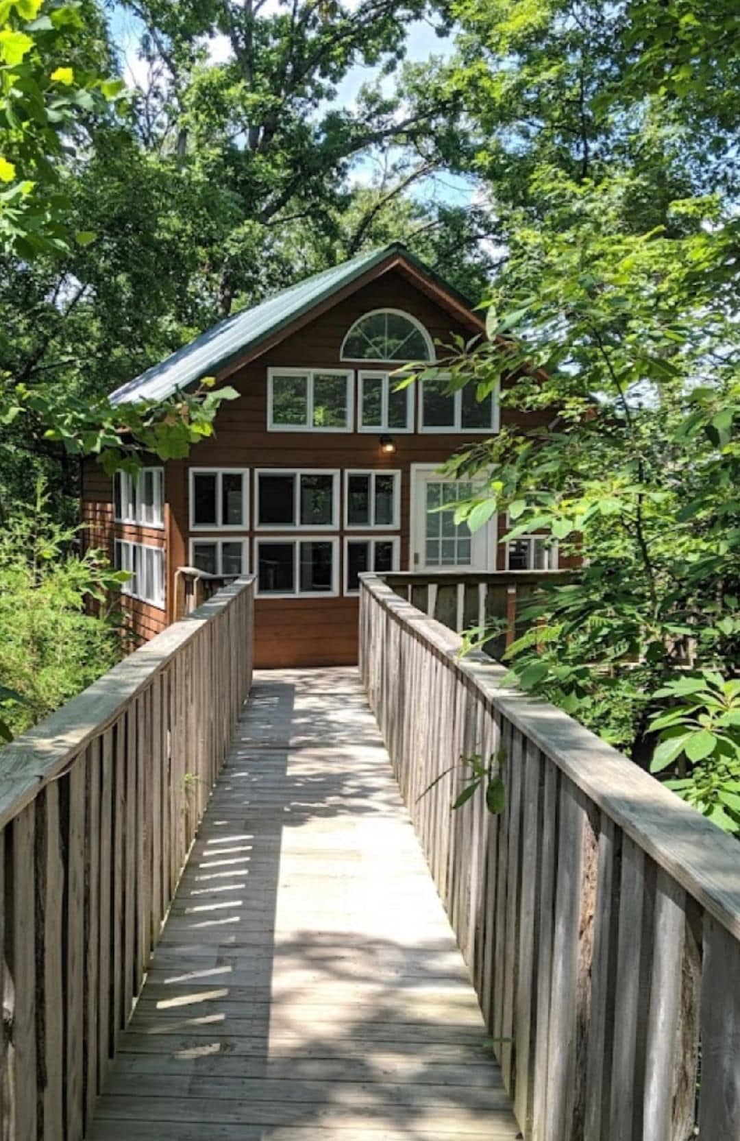 A wooden bridge leading to a two-story house with multiple windows and a covered porch.