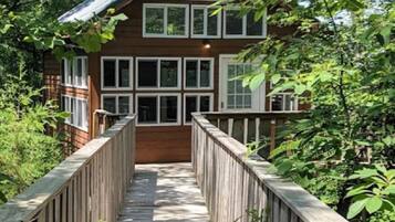 A wooden bridge leading to a two-story house with multiple windows and a covered porch.