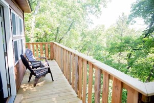 Una terraza de madera con barandilla, una silla y vista a un bosque.