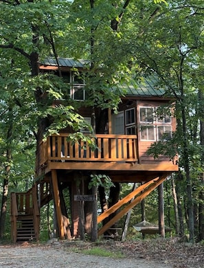 A treehouse with a wooden deck, a staircase, and a sign that reads 'SUNSET'.