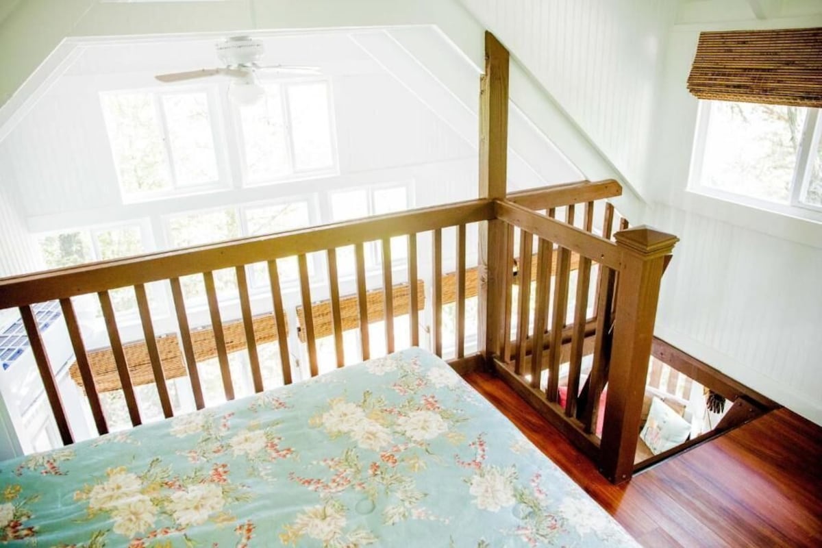 Una habitación con escalera de madera, ventilador de techo y vistas al exterior.