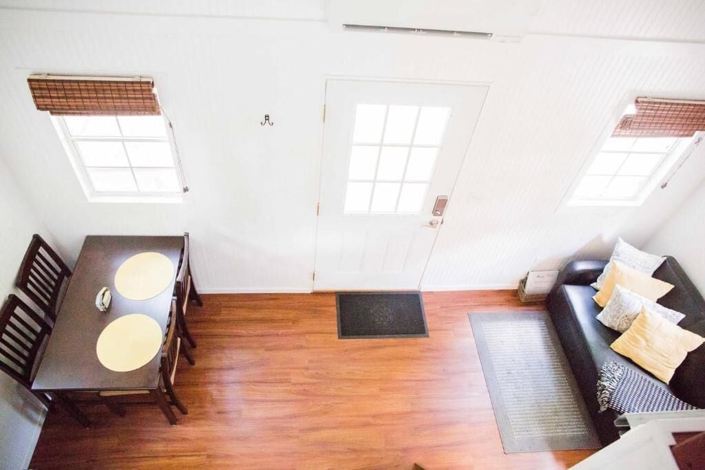 A room with a wooden floor, a dining table with two chairs, a sofa with cushions, and a door with a window.