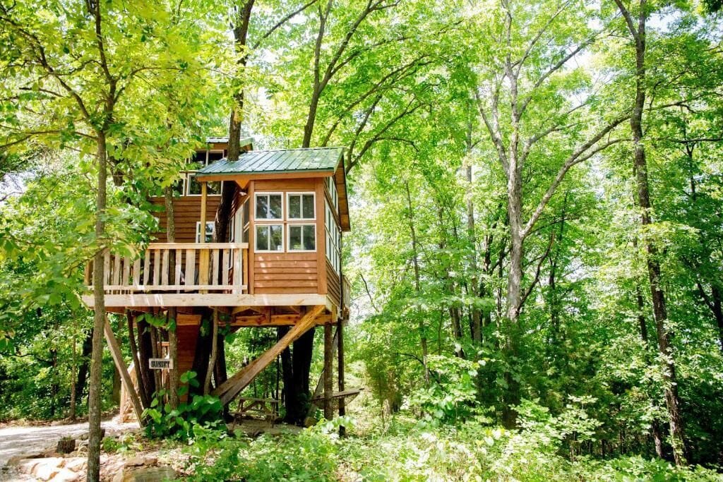 Een houten boomhut met een balkon, omgeven door dicht bos.