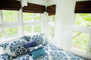 Una habitación con cama, paredes blancas y ventanas con persianas marrones.