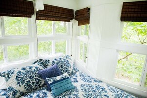 Una habitación con cama, paredes blancas y ventanas con persianas marrones.