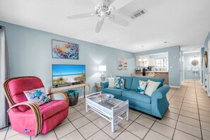 A living room with a red chair, a blue sofa, a coffee table, and a ceiling fan. - New Listing! Master Balcony* 3 Pools* Walk to Sand (Panama City Beach)