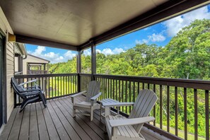 A wooden deck with Adirondack chairs and a table, overlooking a lush green landscape. - New Listing! Master Balcony* 3 Pools* Walk to Sand (Panama City Beach)