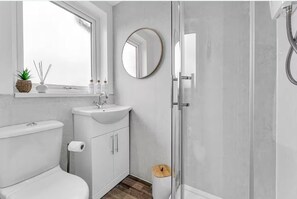 A bathroom with a toilet, sink, mirror, and shower. - 3 Bedroom Leek House Sleep 5 at Peak District (Leek)