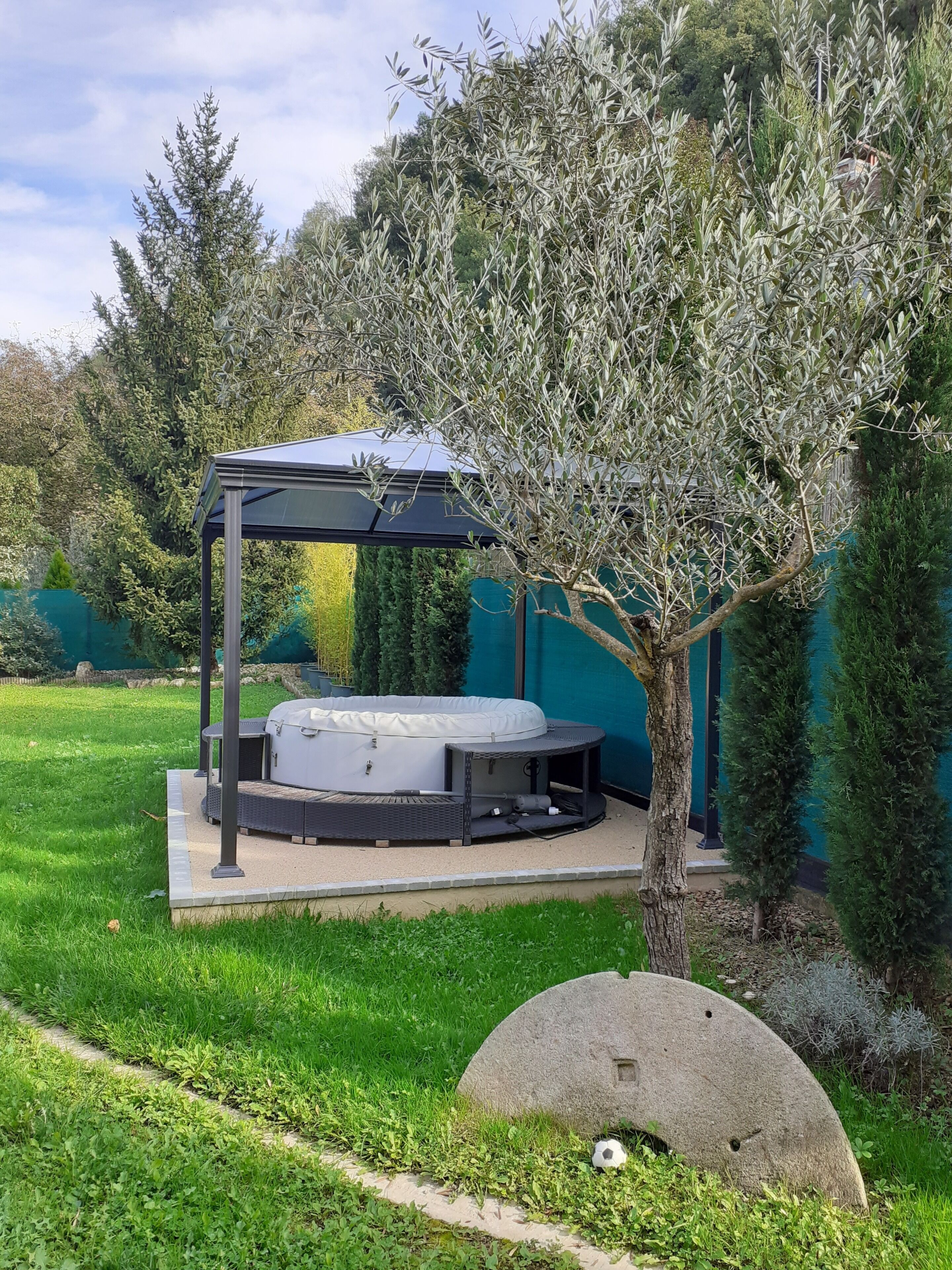 Un espace extérieur aménagé, abrité et doté d’un jacuzzi, entouré de verdure et d’arbres.