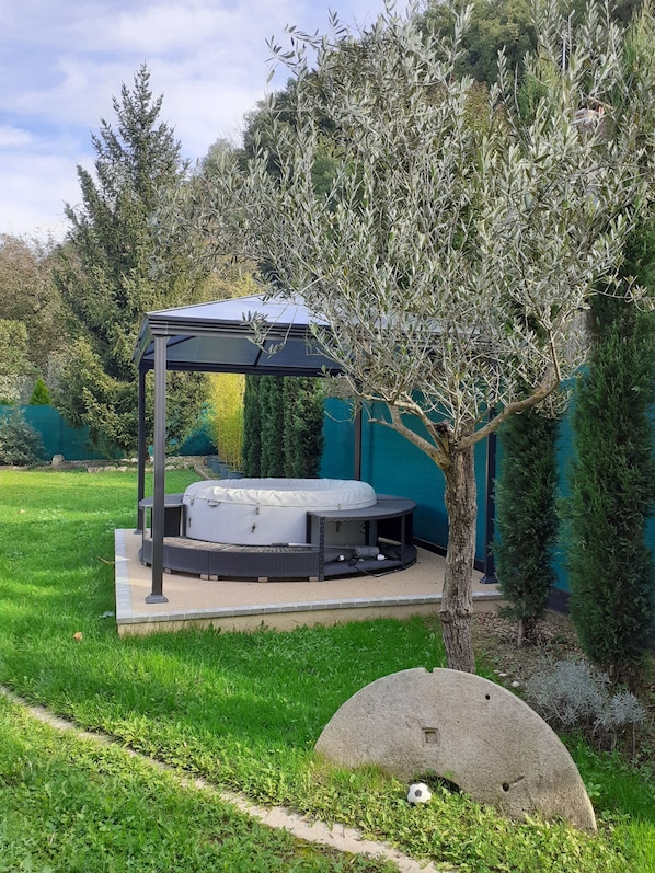 Un espace extérieur aménagé, abrité et doté d’un jacuzzi, entouré de verdure et d’arbres.