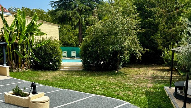 Un'area esterna pavimentata con piscina, immersa nel verde e adiacente a un edificio.
