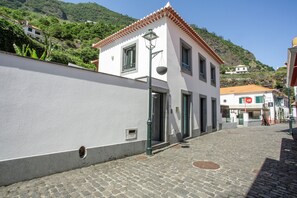Eine enge Kopfsteinpflasterstraße mit einem weißen Gebäude, das ein rotes Ziegeldach, eine Straßenlaterne und eine sichtbare Tür hat.