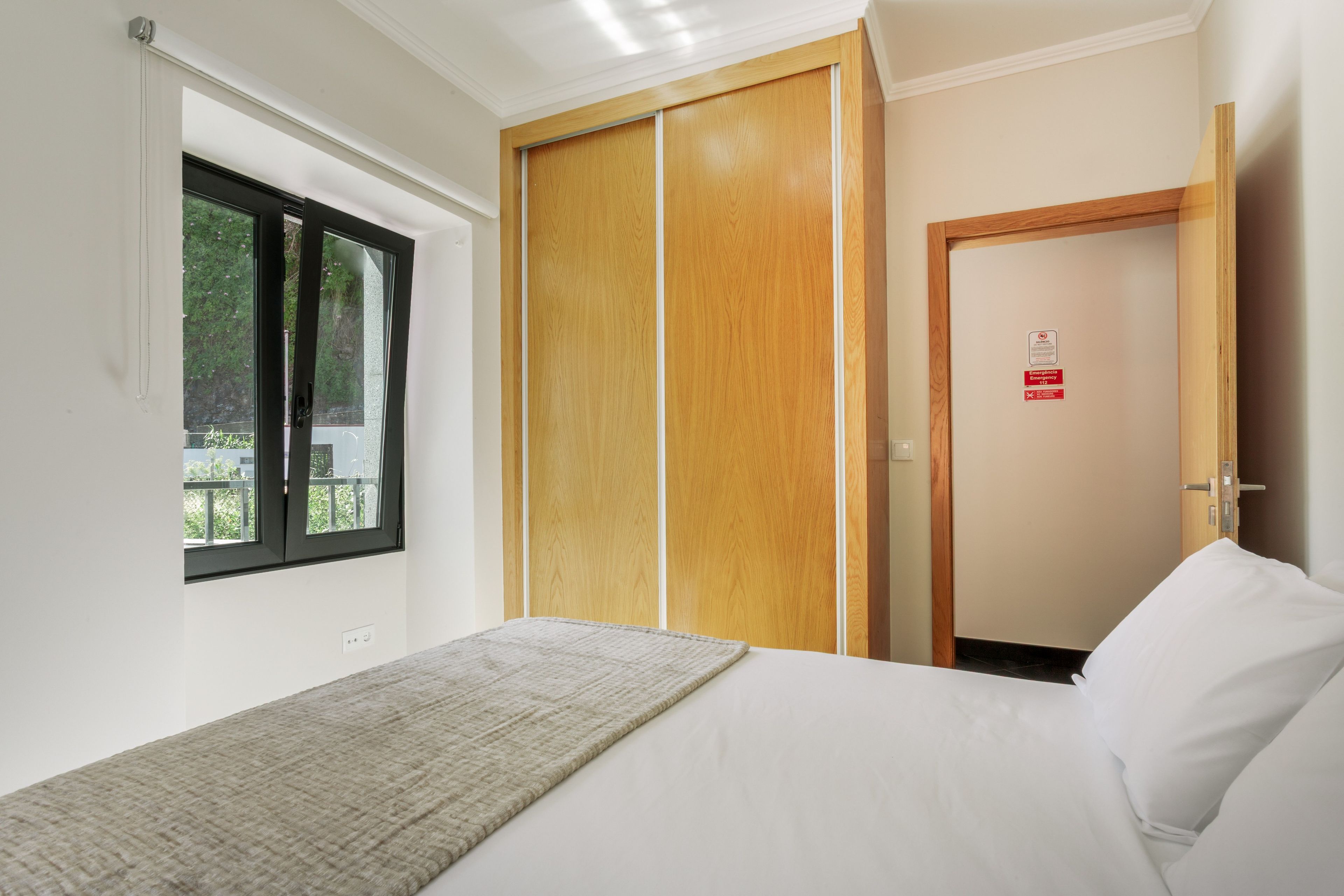 Ein Schlafzimmer mit Bett, Fenster, Kleiderschrank und einer Tür mit einem Notausgangsschild.