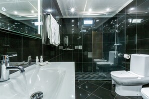 Et moderne badeværelse med et stort, hvidt badekar, et separat toilet og et bruseområde med glasvægge.