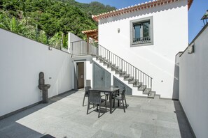 A courtyard with a table and chairs, a staircase, and a white building with a red-tiled roof. - AL - Vic Center House (Sao Vicente)