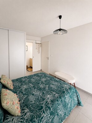 A bedroom with a bed, a bench, a wardrobe, and a door leading to another room. - New apartment, terrace & parking – Résidence Boréal, Montpellier (Monptellier)