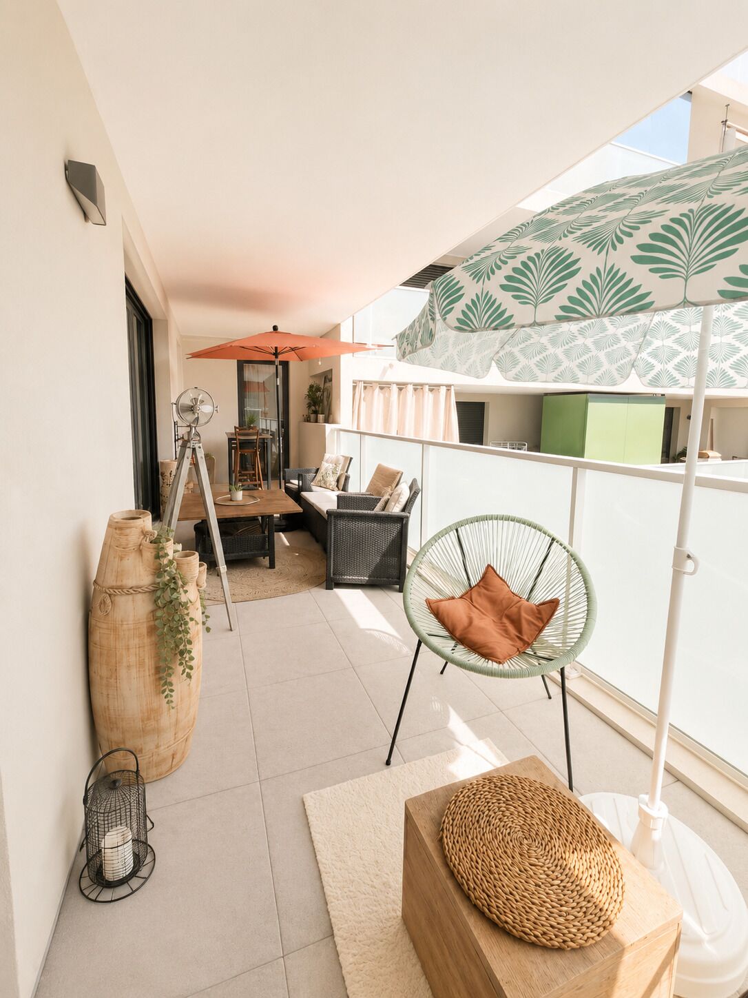 Un balcon avec une chaise en osier, une table en bois, un grand vase et un tabouret en fibres tressées.