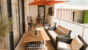 Ein Balkon mit Holztisch, Korbmöbeln und einem großen orangefarbenen Sonnenschirm.