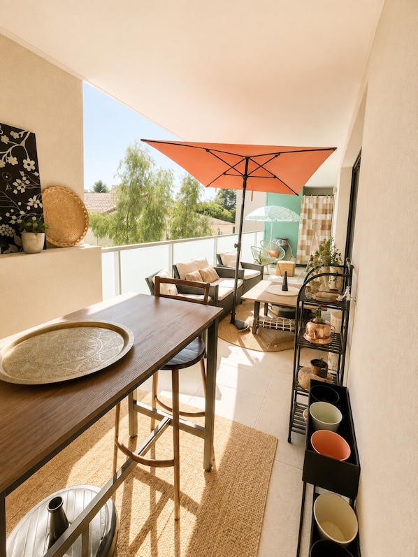 A balcony with a wooden table, chairs, a metal shelf with pots, and an orange umbrella. - New apartment, terrace & parking – Résidence Boréal, Montpellier (Monptellier)